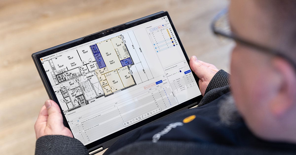 Henkilö pitää kädessään tablettia, jossa näkyy pohjakuva rakennuksesta. Kuvassa näkyvä ohjelmisto on Admicom Quantima -määrälaskentaratkaisu.